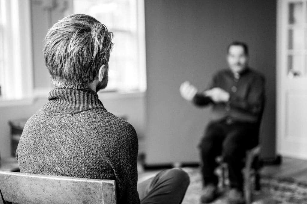 Back of a man listening attentively during a Big Talk conversation, with another person gesturing in the background