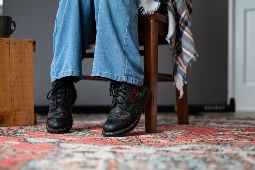 Close-up of a seated person’s crossed legs and black boots with red embroidery, captured during a Big Talk session