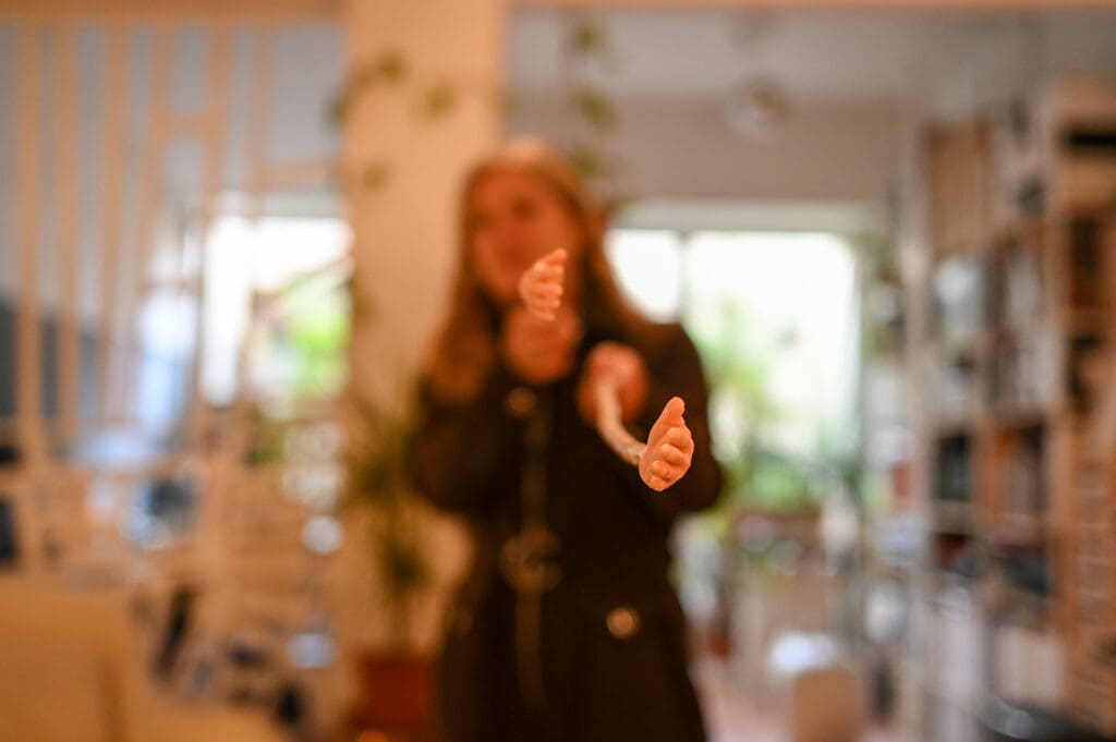 Out-of-focus woman holding out two sculpted hands toward the camera in a warmly lit room