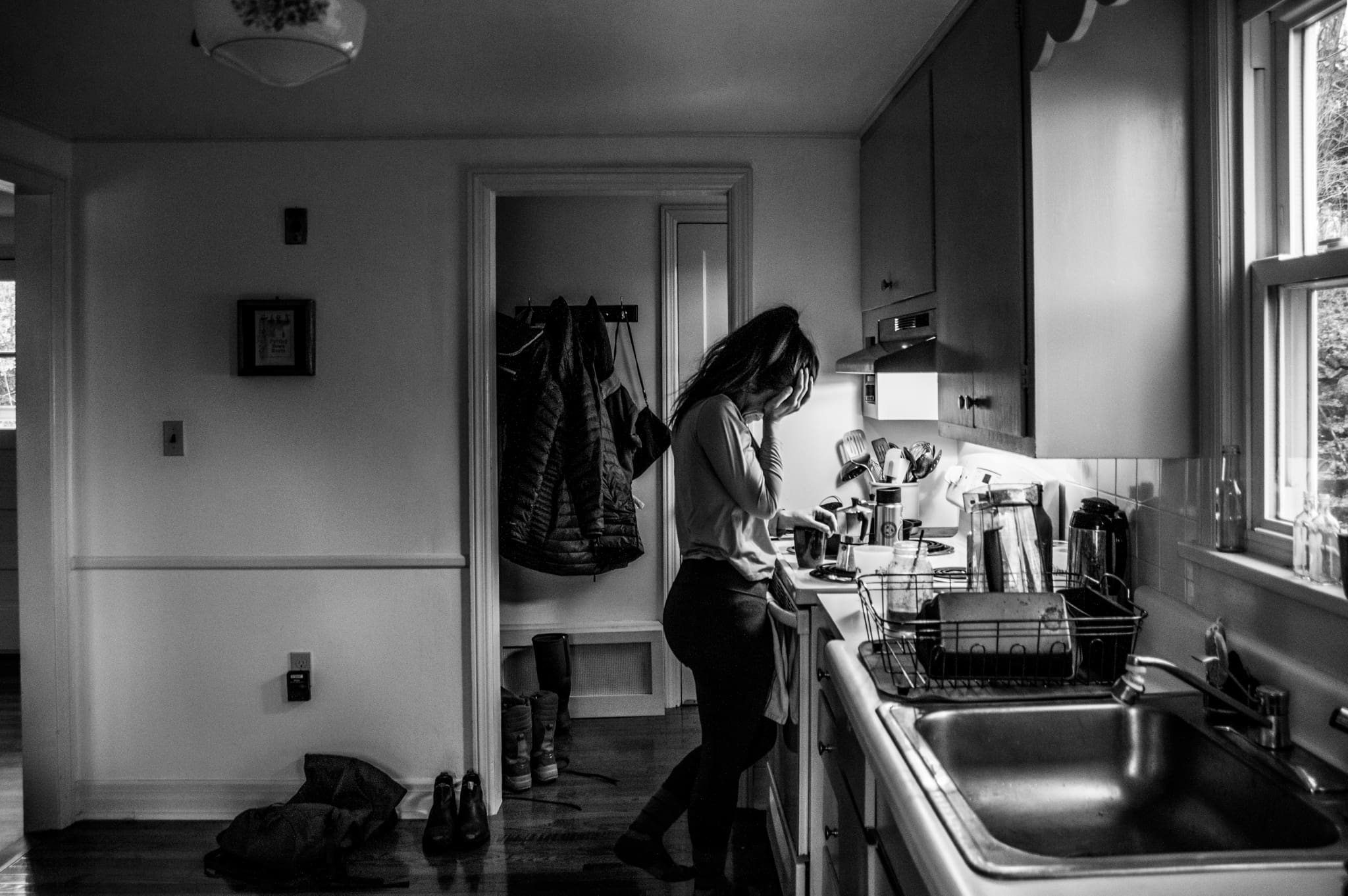 Woman standing at a kitchen stove with her hand on her face, surrounded by daily mess.