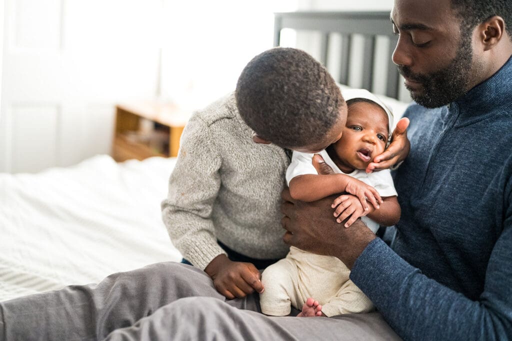 Older sibling giving newborn a kiss during photo session