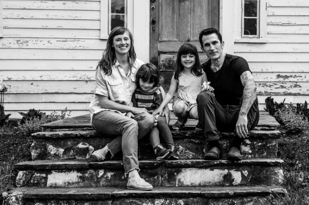Black and white photo of a family sitting on their front steps, smiling warmly together.