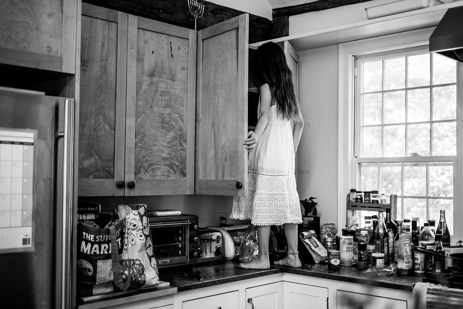 young child climbing kitchen counter to peek inside cupboard during candid family photo session