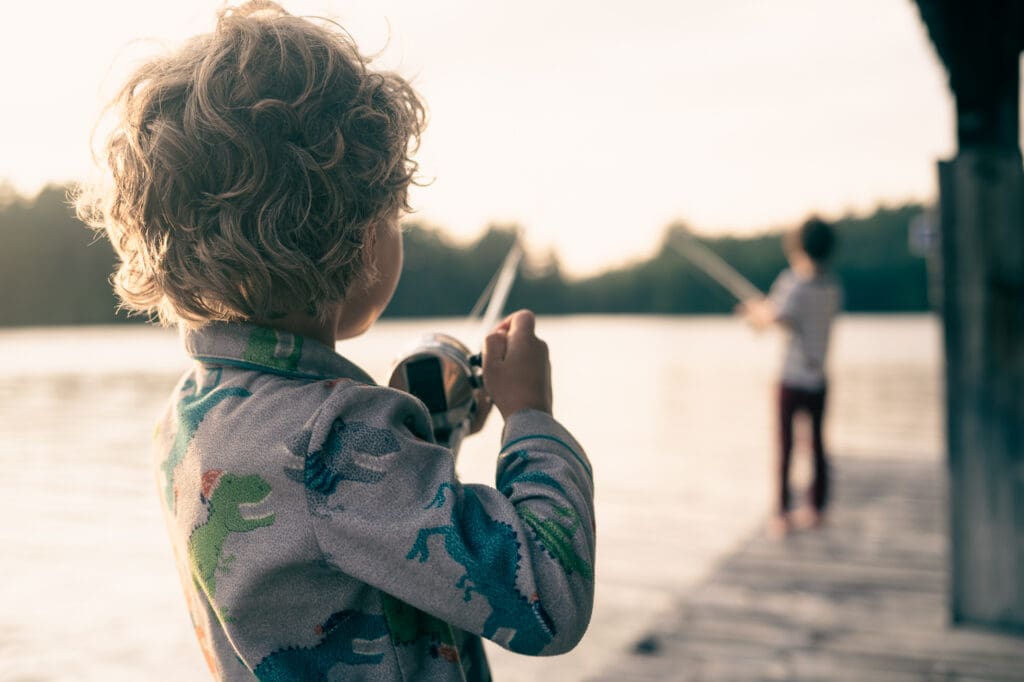 Young child holding a fishing rod on a dock at sunset
