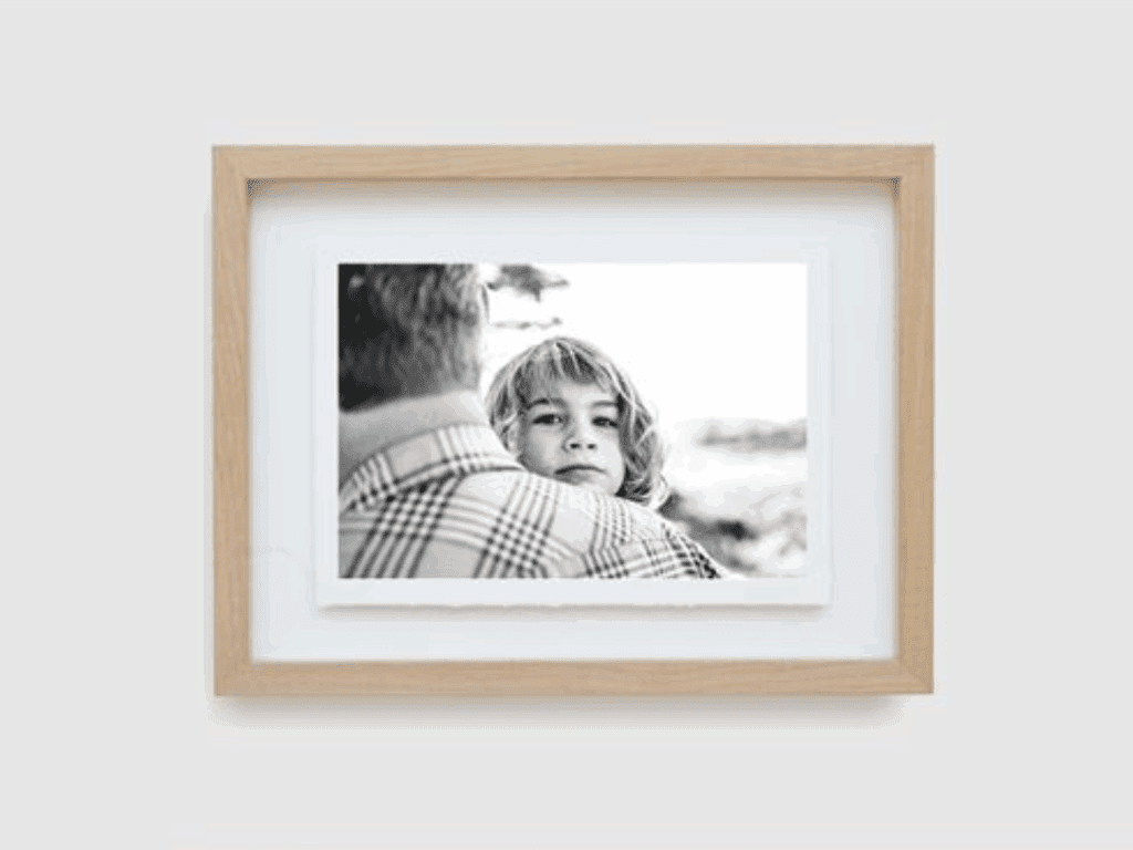 Black-and-white photo of a child framed in a natural wood float frame with a deckled edge print