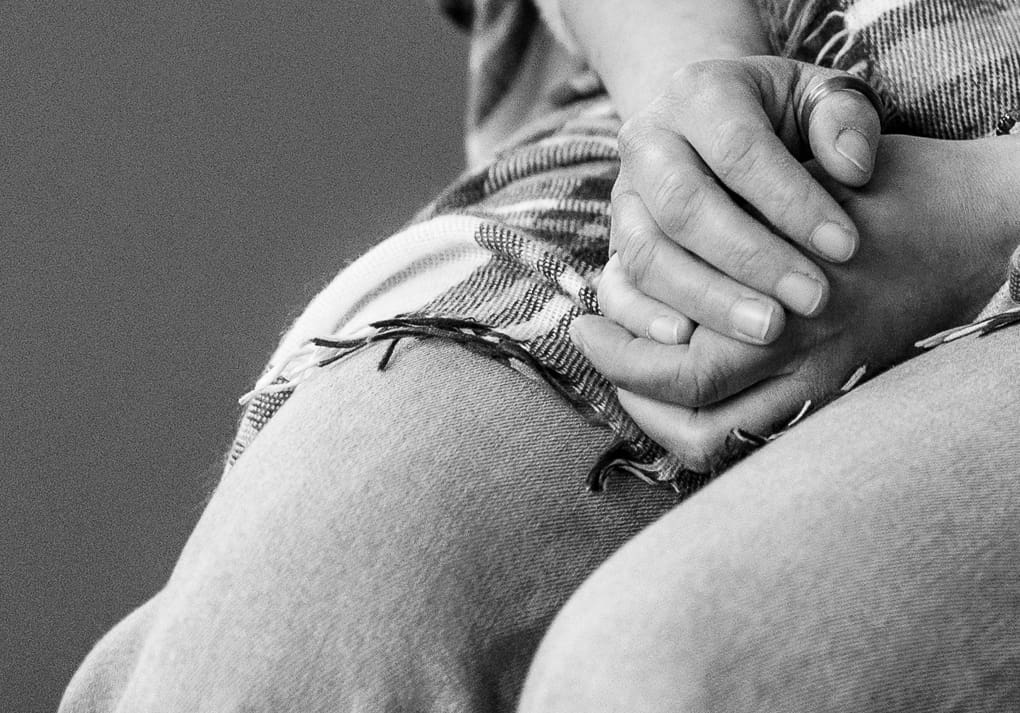 A black and white close-up of two hands gently clasped in a lap during a documentary-style portrait session