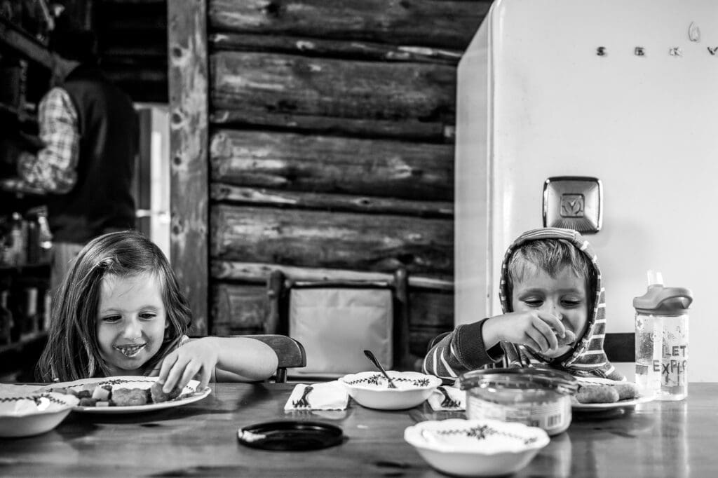 Two young children eating at a wooden table in a cozy cabin