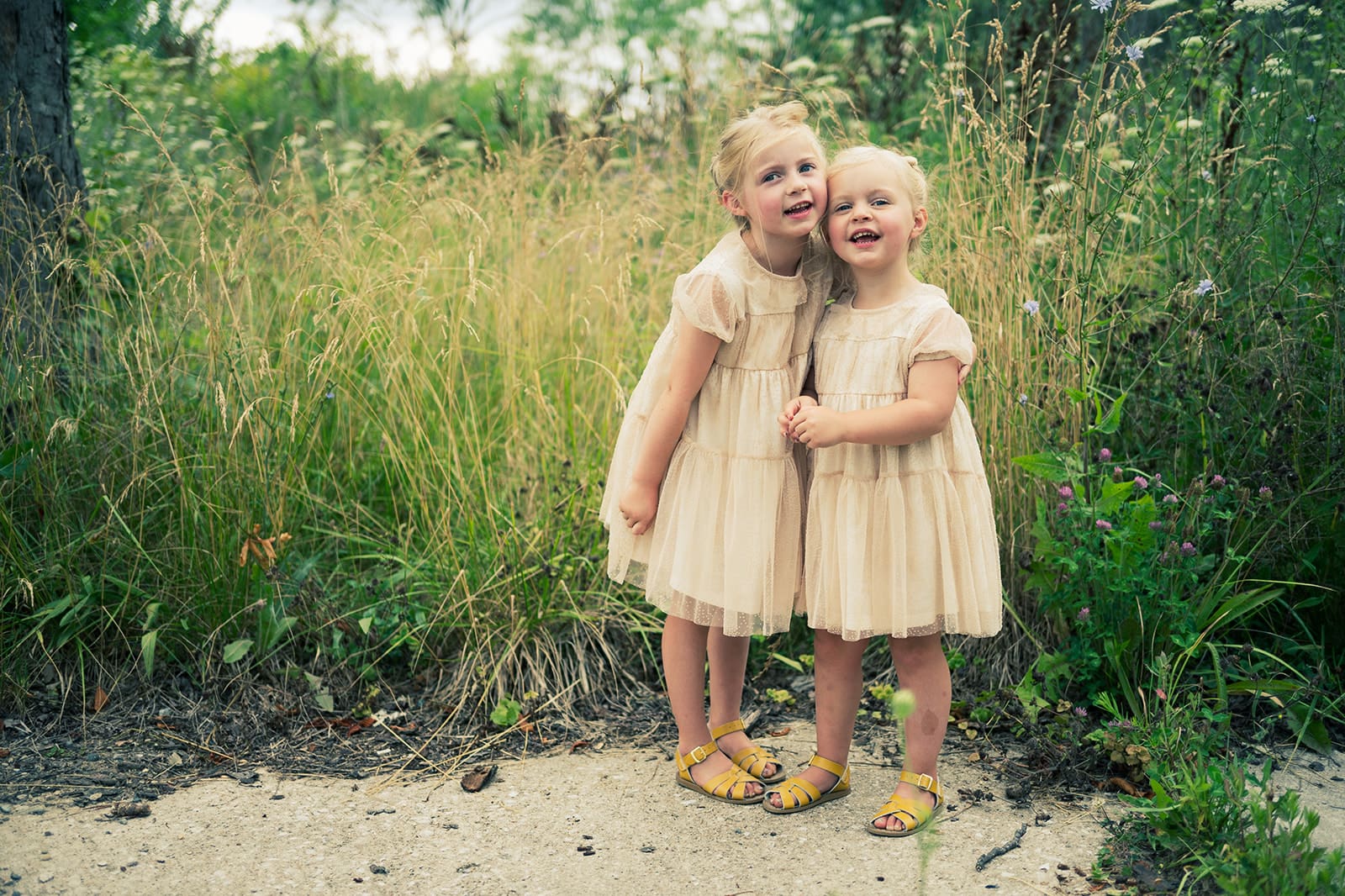 Two young sisters in matching cream dresses smiling together outdoors during fall family mini session