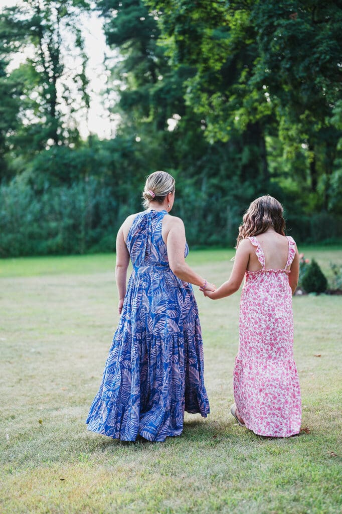 Mother and daughter holding hands walking through grassy field during fall family portrait session