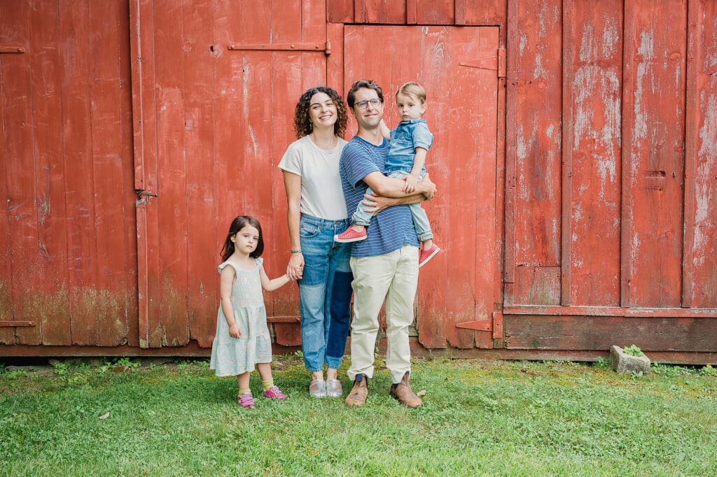 A family during a 10-minute mini portrait session standing in front of a rustic red barn