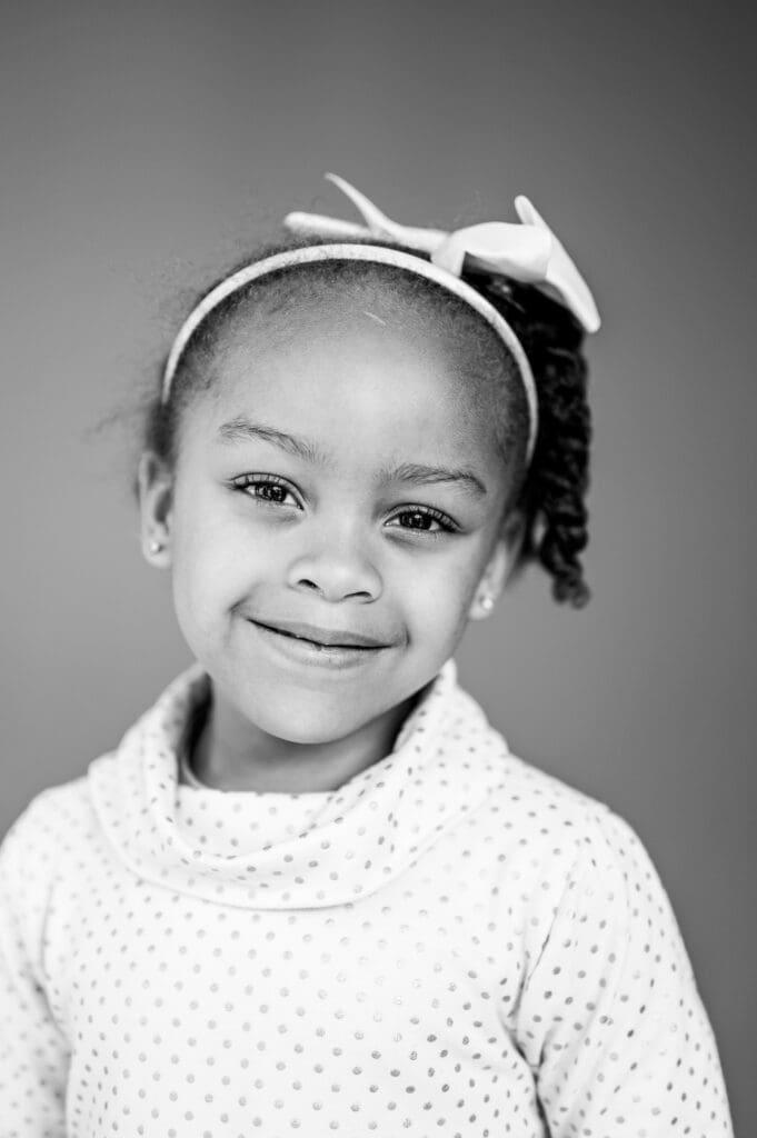 Black and white school portrait of girl with bow headband smiling naturally, by Rebecca Bloomfield Photography