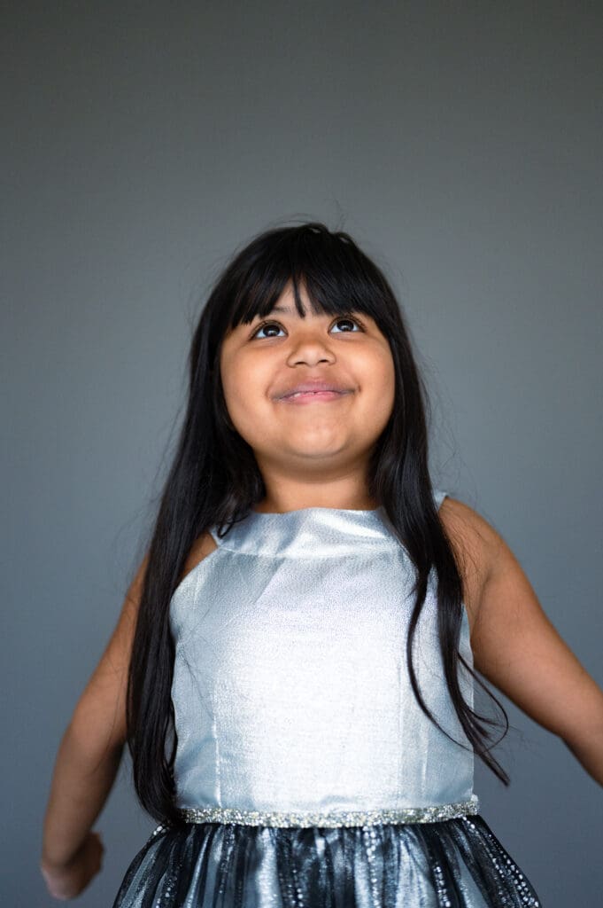Fine art school portrait of young girl in silver dress looking up and smiling, by Rebecca Bloomfield Photography