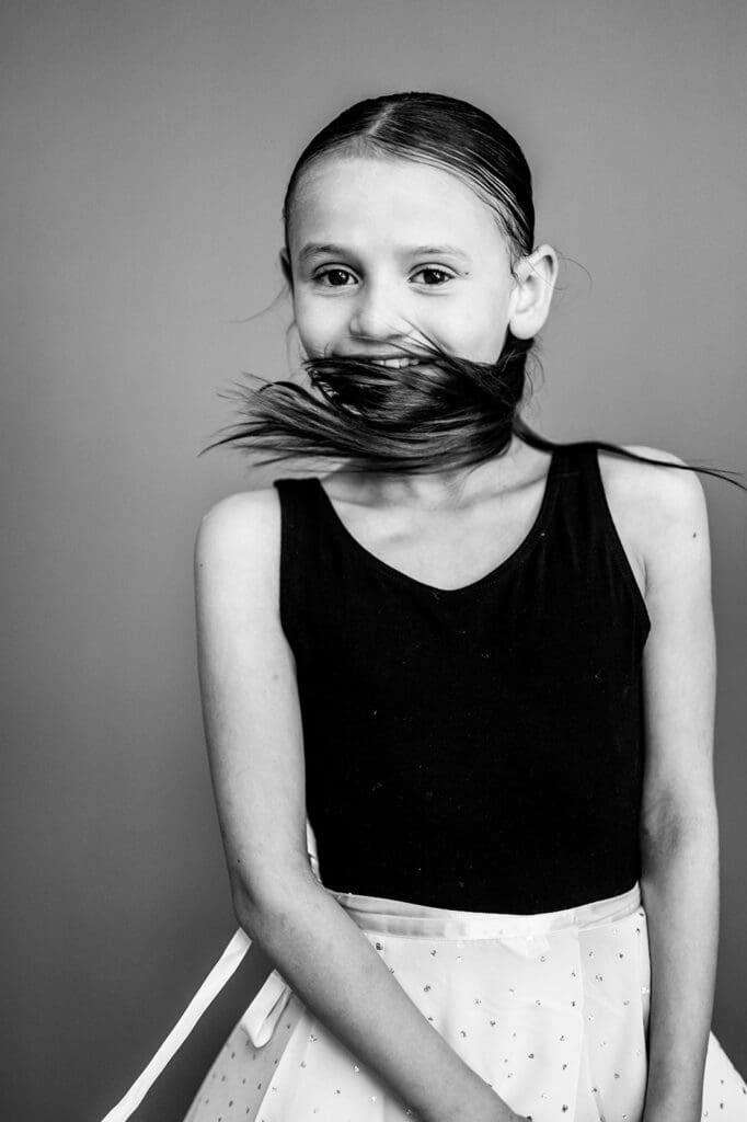 Black and white school portrait of girl smiling with hair blowing across face, photographed by Rebecca Bloomfield Photography