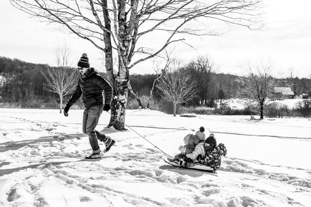 parent pulling children on a sled while kids stay focused on the activity rather than the camera 