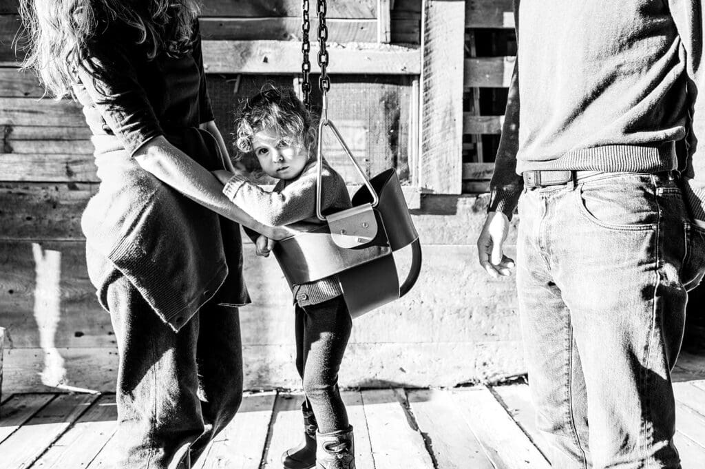 A toddler standing in a swing while being supported by parents during a lifestyle family photography session