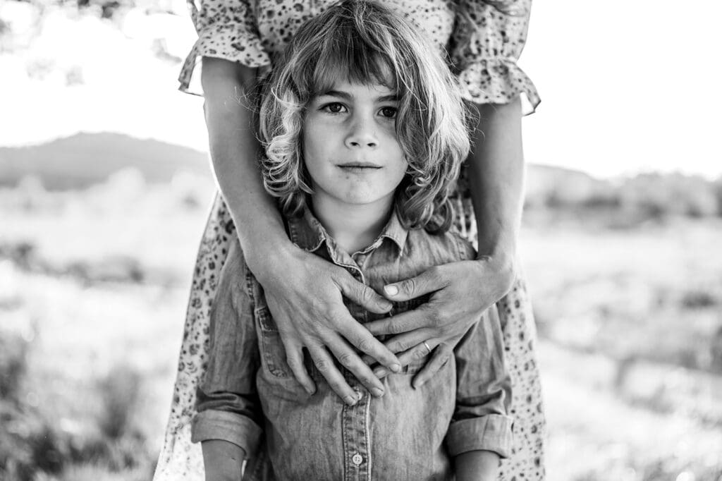 child standing outdoors with parent hands around them during a candid family photo session