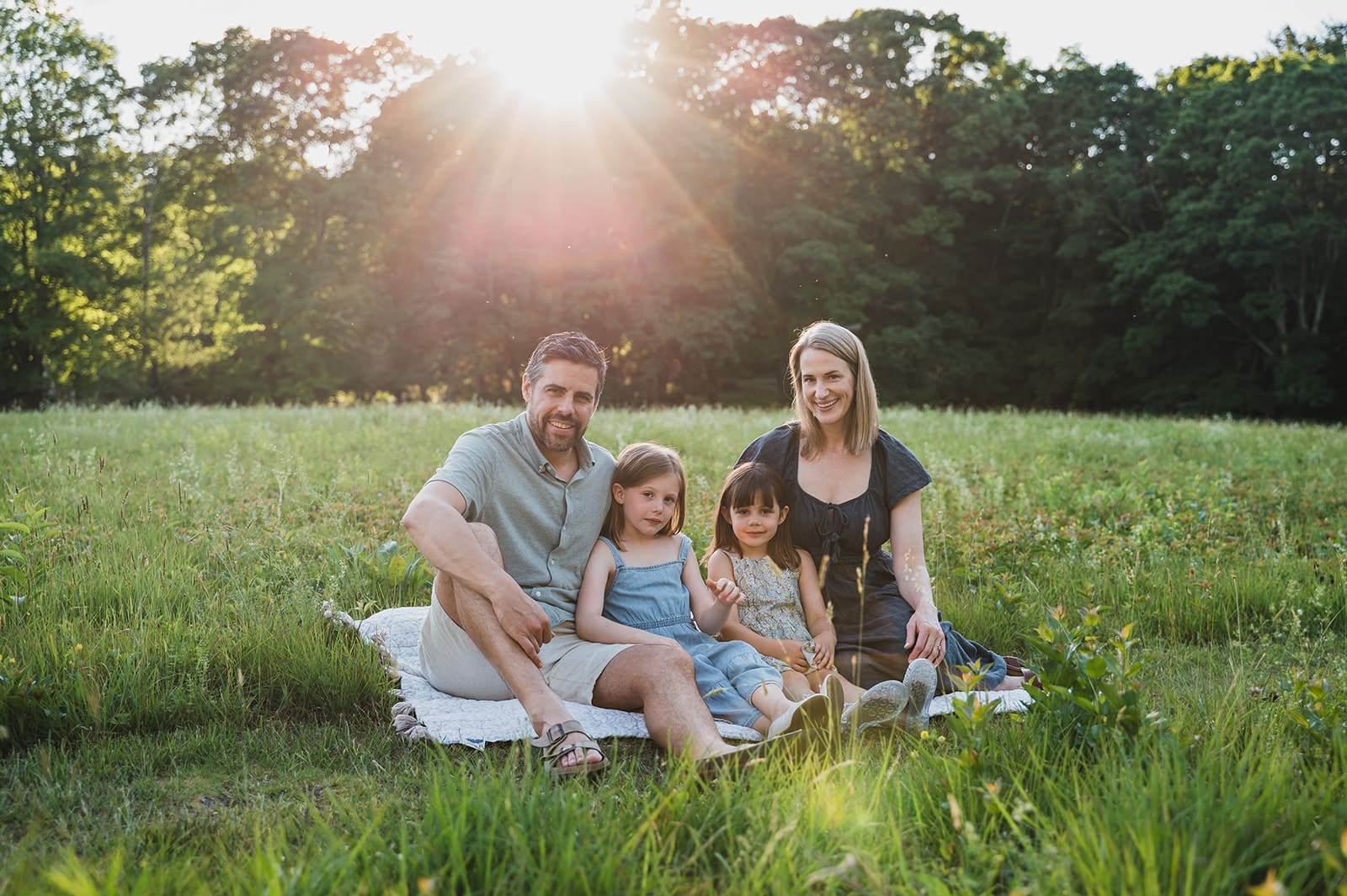 A family of four sits on a blanket snuggled in to each other at sunset during a short and sweet family photo session