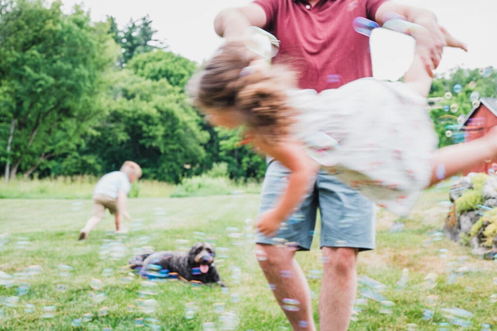 father swinging daughter through bubbles during Hudson Valley family vacation session