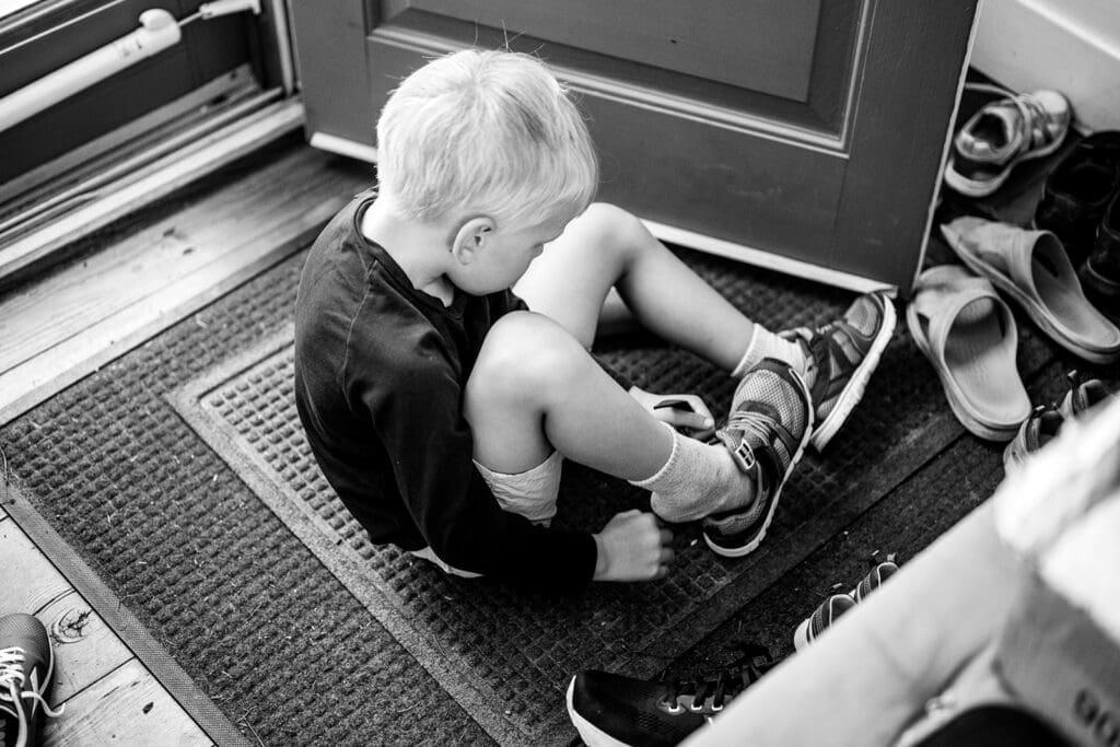 Toddler sitting on a doormat putting on shoes during a candid family photography session