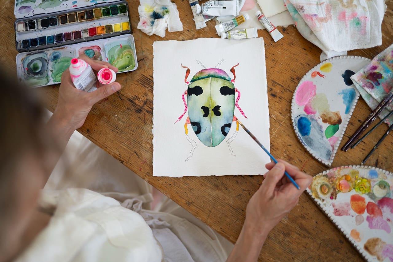 artist painting a watercolor portrait at her workspace